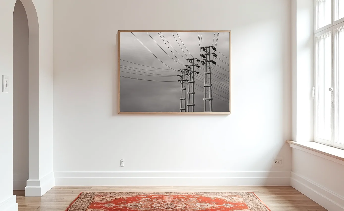 Bulutlu gökyüzü önünde sıralanan üç elektrik direği, kablolarla derinlik oluşturan çağdaş sanat fotoğrafı.