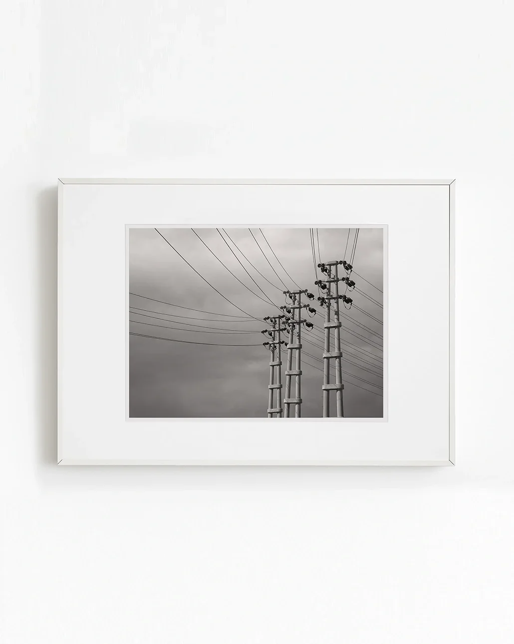 Endüstriyel peyzaj içinde yan yana konumlanan üç elektrik direği, çizgisel kablolarla güçlü perspektif sunan duvar sanatı fotoğrafı.