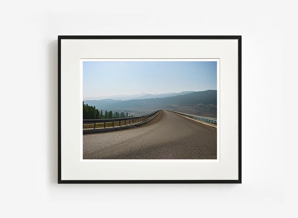 Asfalt yol, uzak dağ silsilesi ve gökyüzü ilişkisini sade kompozisyonla aktaran sanatsal fotoğraf çalışması.